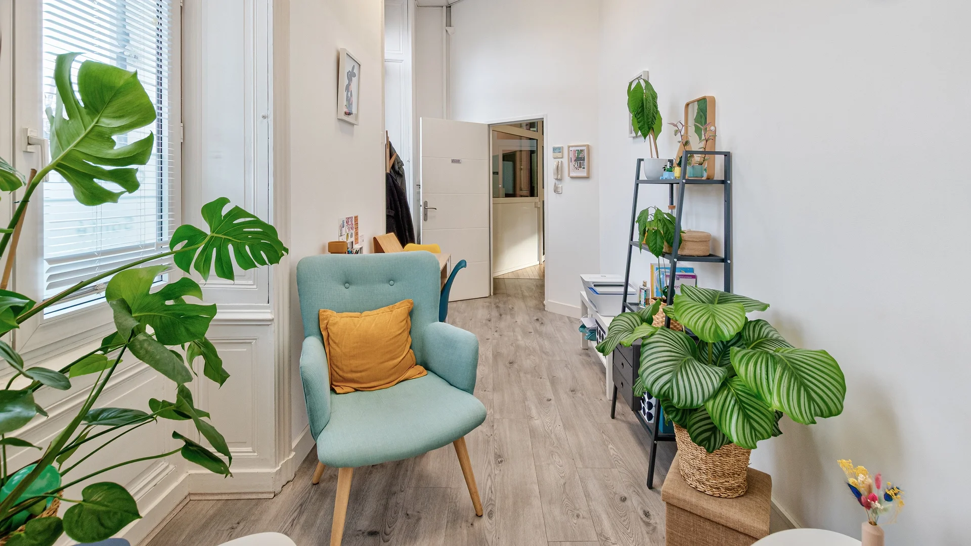 Vue de l'entrée du cabinet de santé à Nantes Mellinet avec fauteuil scandinave bleu, parquet clair et décoration végétale apaisante.