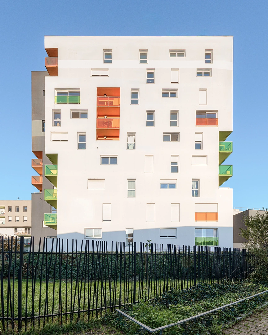 Immeuble résidentiel Chroma à Nantes montrant une façade blanche avec des fenêtres asymétriques et des balcons colorés en verre orange et vert.