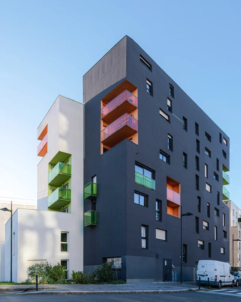 Vue en angle du projet Chroma à Nantes montrant une façade anthracite imposante juxtaposée à un volume blanc, avec des balcons en verre vert et orange.