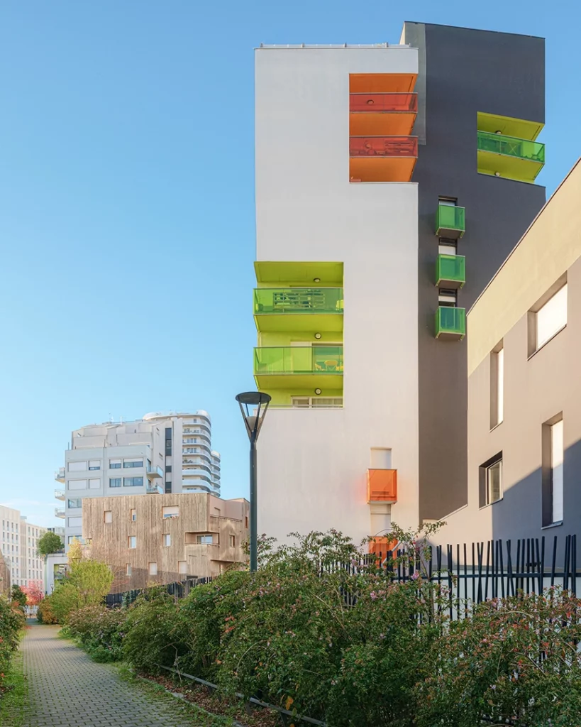 Immeuble Chroma à Nantes vu depuis un sentier végétalisé, mettant en avant les balcons en saillie vert acide et orange sur des façades contrastées.