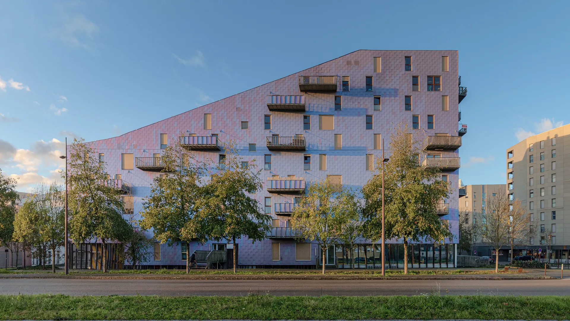 Vue extérieure de l'immeuble Le Ruban à Nantes, présentant sa façade asymétrique et ses balcons filants en béton sous un ciel bleu.