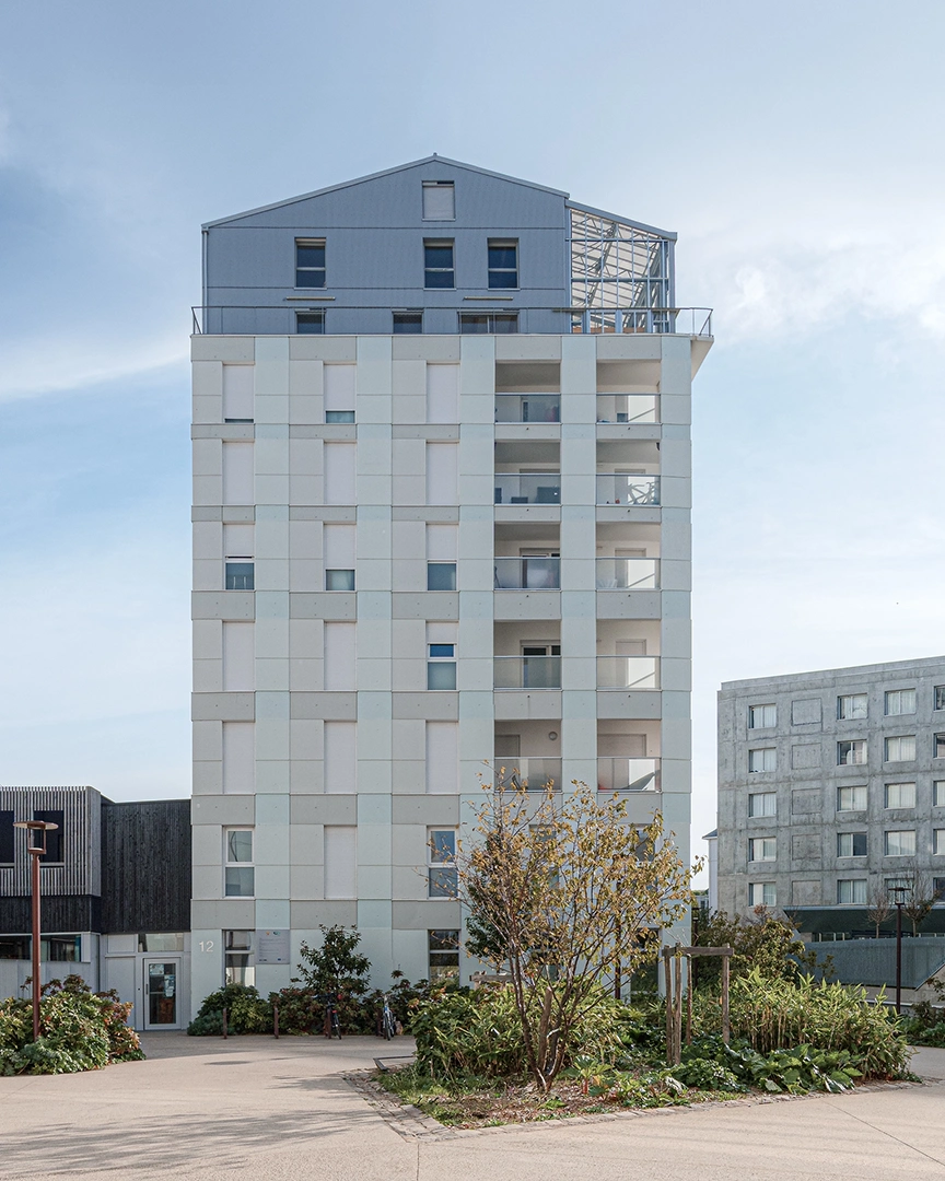Façade verticale d'un immeuble de 7 étages aux 5 Ponts, Nantes. Le bâtiment présente des panneaux de façade blancs et gris clair, des balcons filants à droite, et est surmonté d'un attique en métal gris avec une serre vitrée sous un toit à double pente.