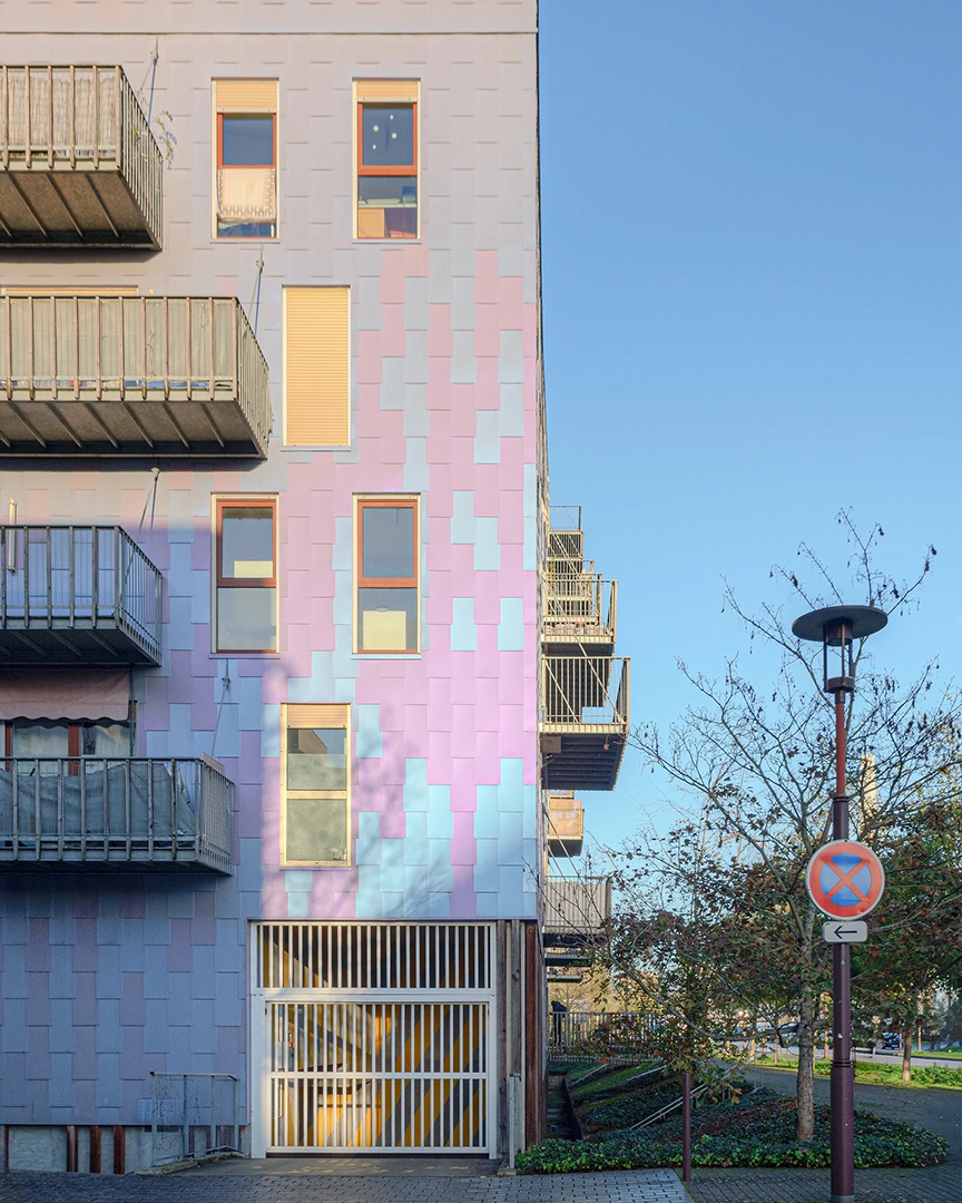Gros plan sur la façade de l'immeuble Le Ruban à Nantes montrant un motif de panneaux rectangulaires aux nuances dégradées de bleu, violet et rose, avec des balcons métalliques et une entrée de parking sécurisée.
