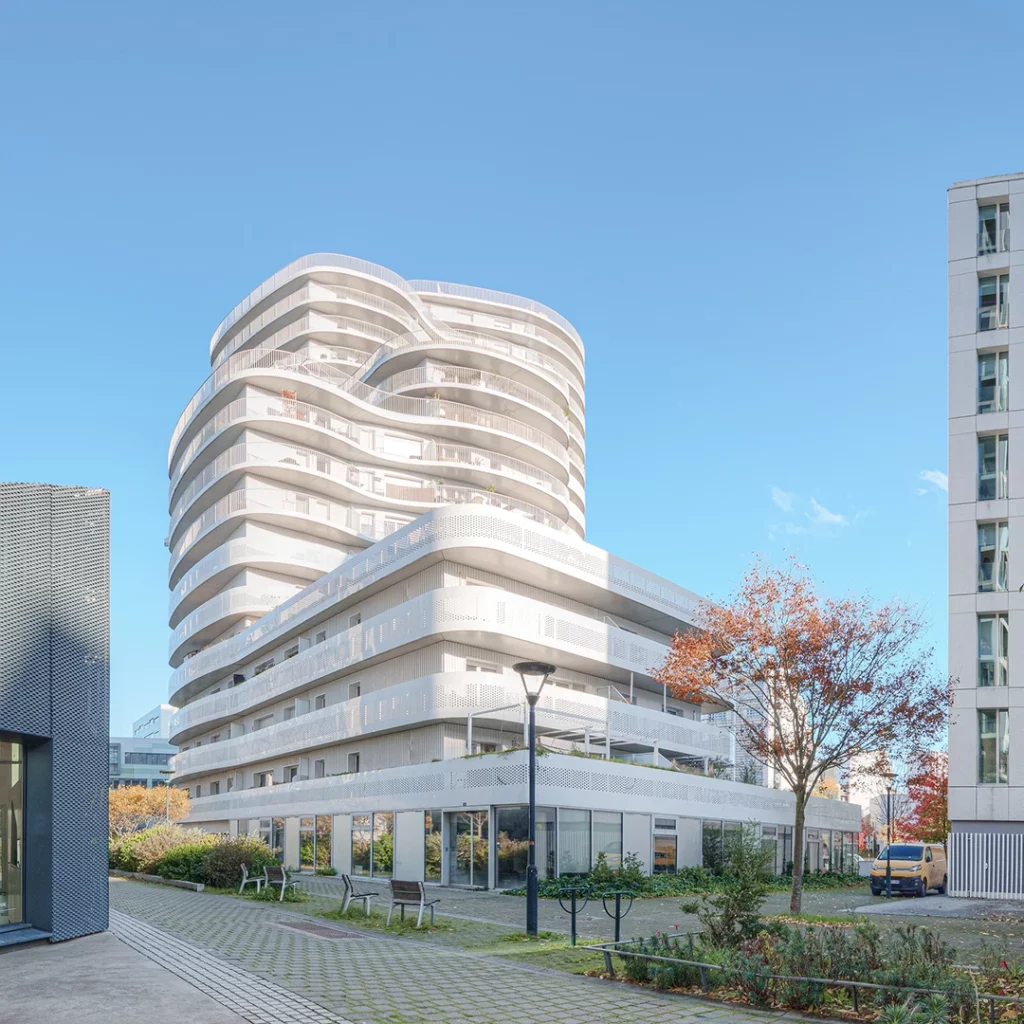 Photographie d'architecture latérale de l'immeuble New'R à Nantes, montrant le parvis piéton, les commerces en rez-de-chaussée et l'empilement décalé des terrasses courbes.
