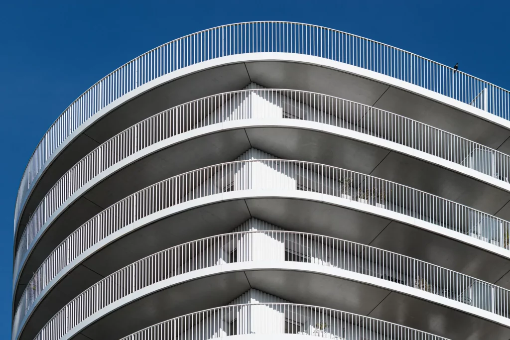 Gros plan abstrait sur la répétition des balcons courbes blancs et des garde-corps métalliques fins de l'immeuble New'R à Nantes, sur un fond de ciel bleu uni.