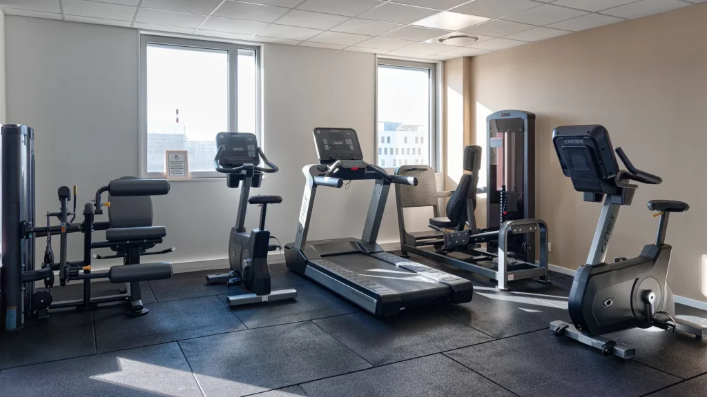 Salle de sport et rééducation d'un cabinet de kinésithérapie à Nantes. Vue sur des équipements Cybex : tapis de course, vélo de biking et machines de renforcement musculaire sur sol technique noir.