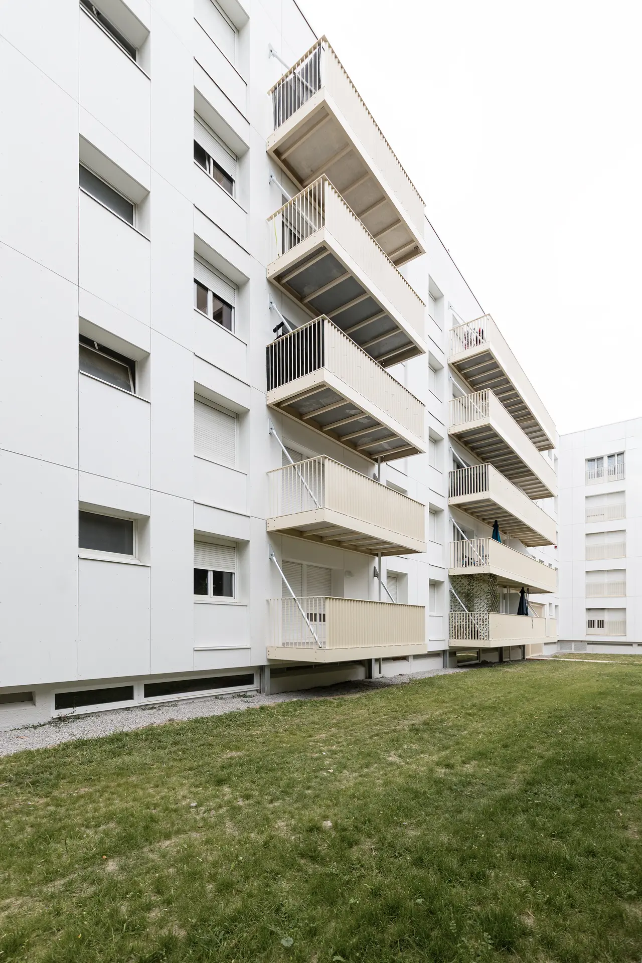 Photo d'architecture montrant le détail des balcons suspendus à tirants métalliques fixés sur la façade blanche d'un immeuble NMH.