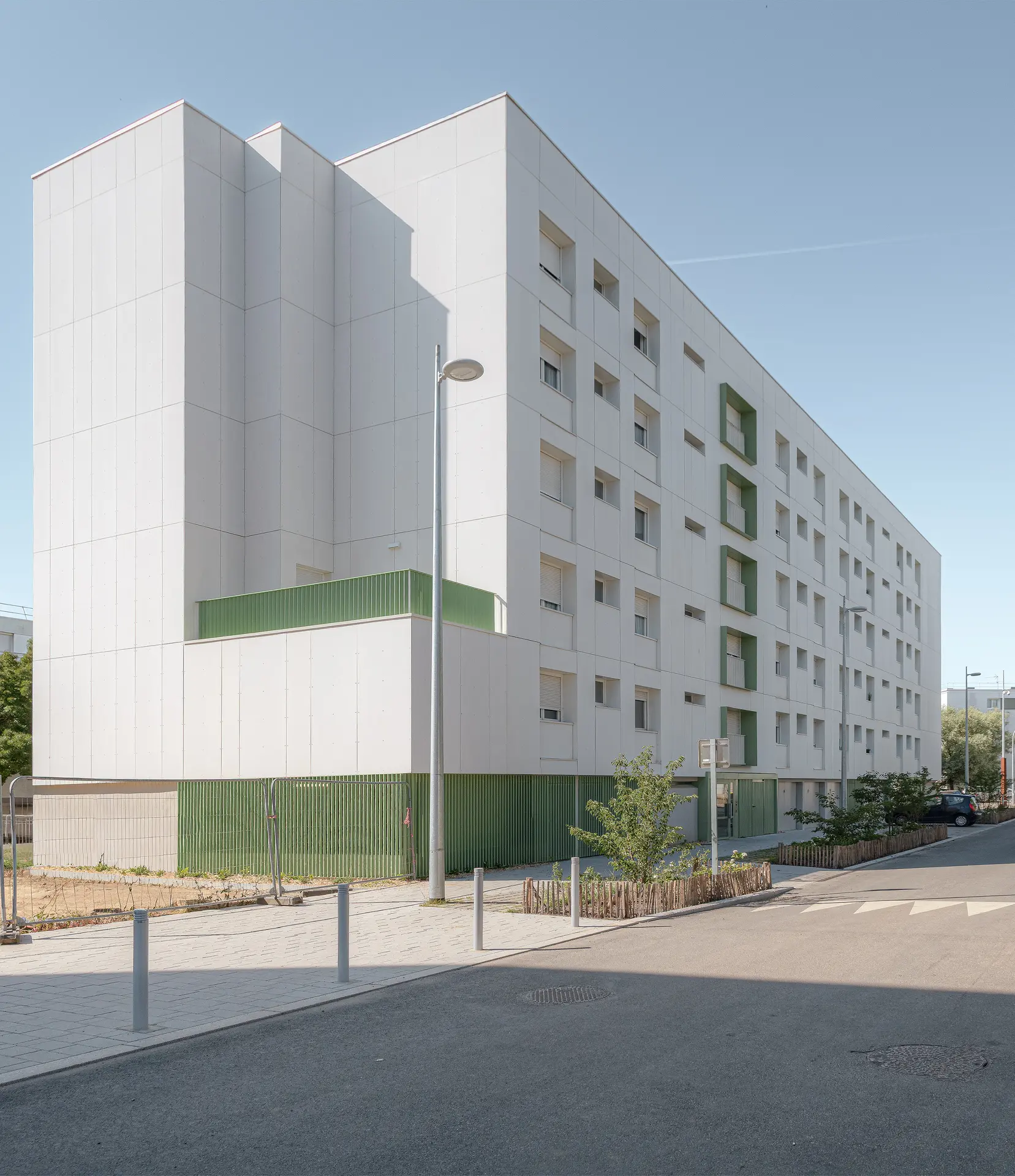 Vue extérieure d'un bâtiment de logements sociaux modernisé à Nantes par l'agence d'architecture Jba, avec un socle vert et un lampadaire.