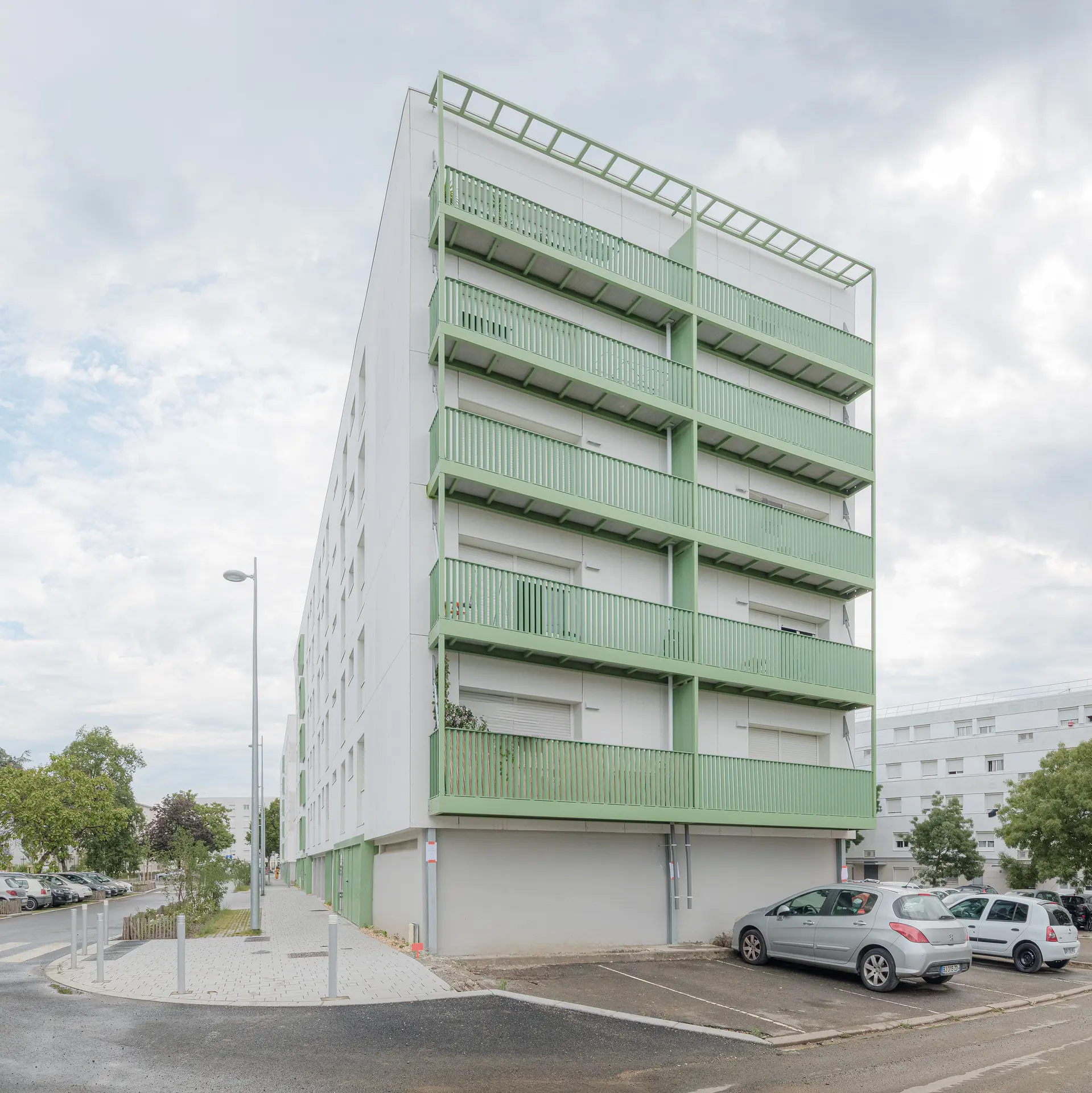 Zoom sur l'angle d'une copropriété réhabilitée affichant de grands balcons filants à structure verte, projet d'architecture à Nantes.