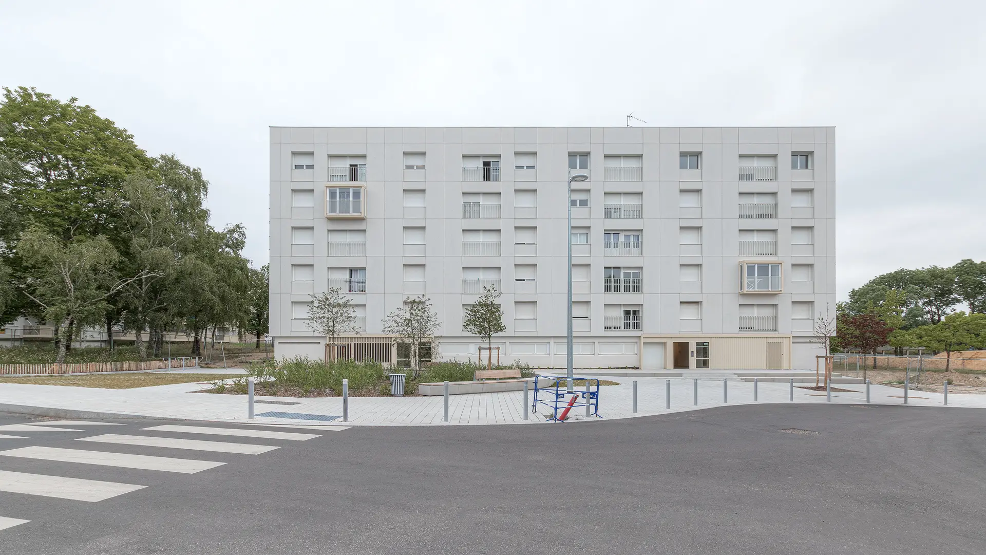 Vue d'ensemble de la façade principale d'un bâtiment réhabilité aux normes BBC Effinergie avec parvis piétonnier et bow-windows, agence Jba.