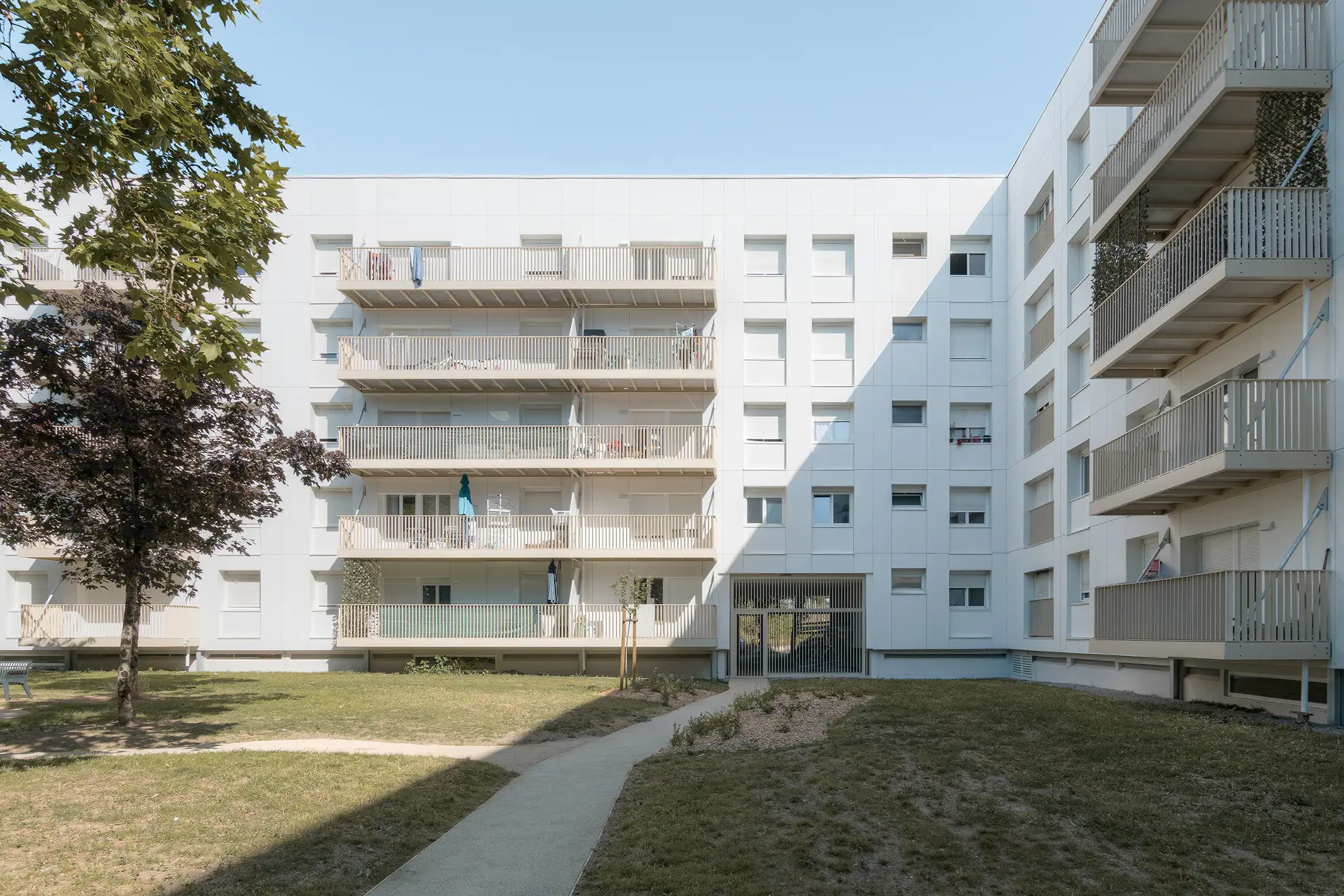 Vue depuis le cœur d'îlot en pelouse montrant les façades en équerre équipées de balcons et de loggias protectrices, signées Jba.